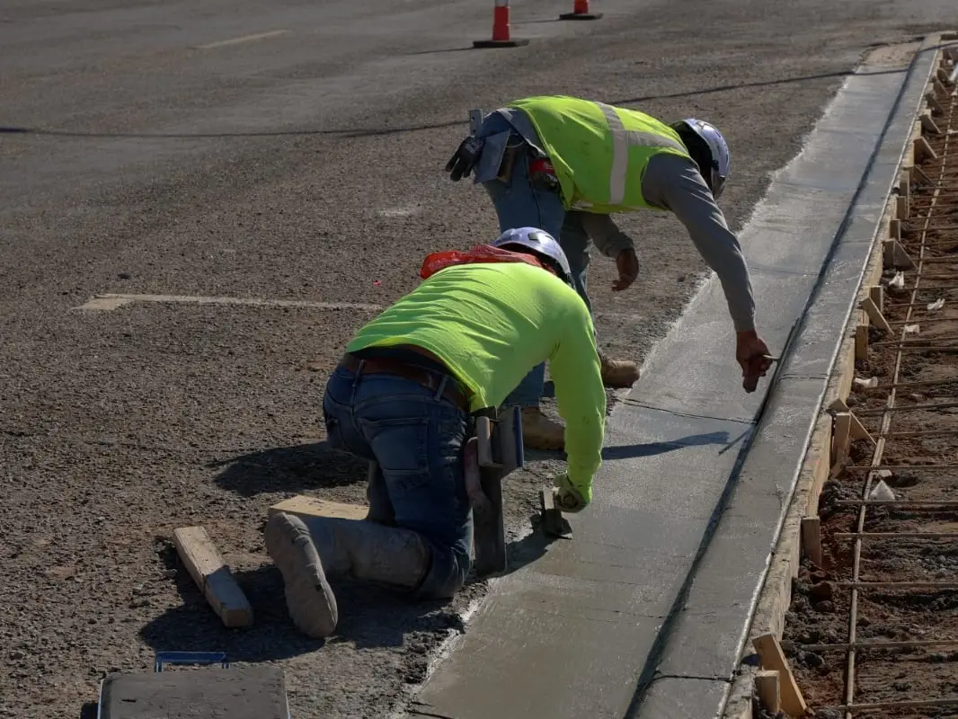 Two crew members hand-finishing a freshly placed concrete curb and gutter along a street