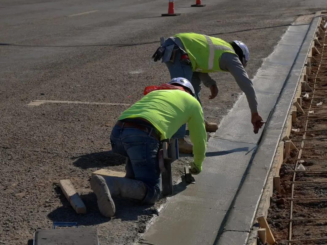Two crew members hand-finishing a freshly placed concrete curb and gutter along a street