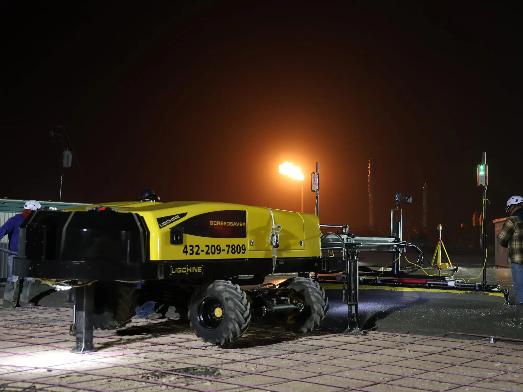 A screed machine leveling a concrete slab pour at night under work lights