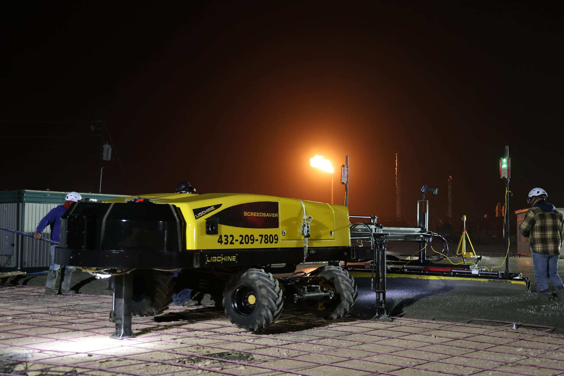 Precision Screeding screed machine on a slab pour at night, with crew members at each end