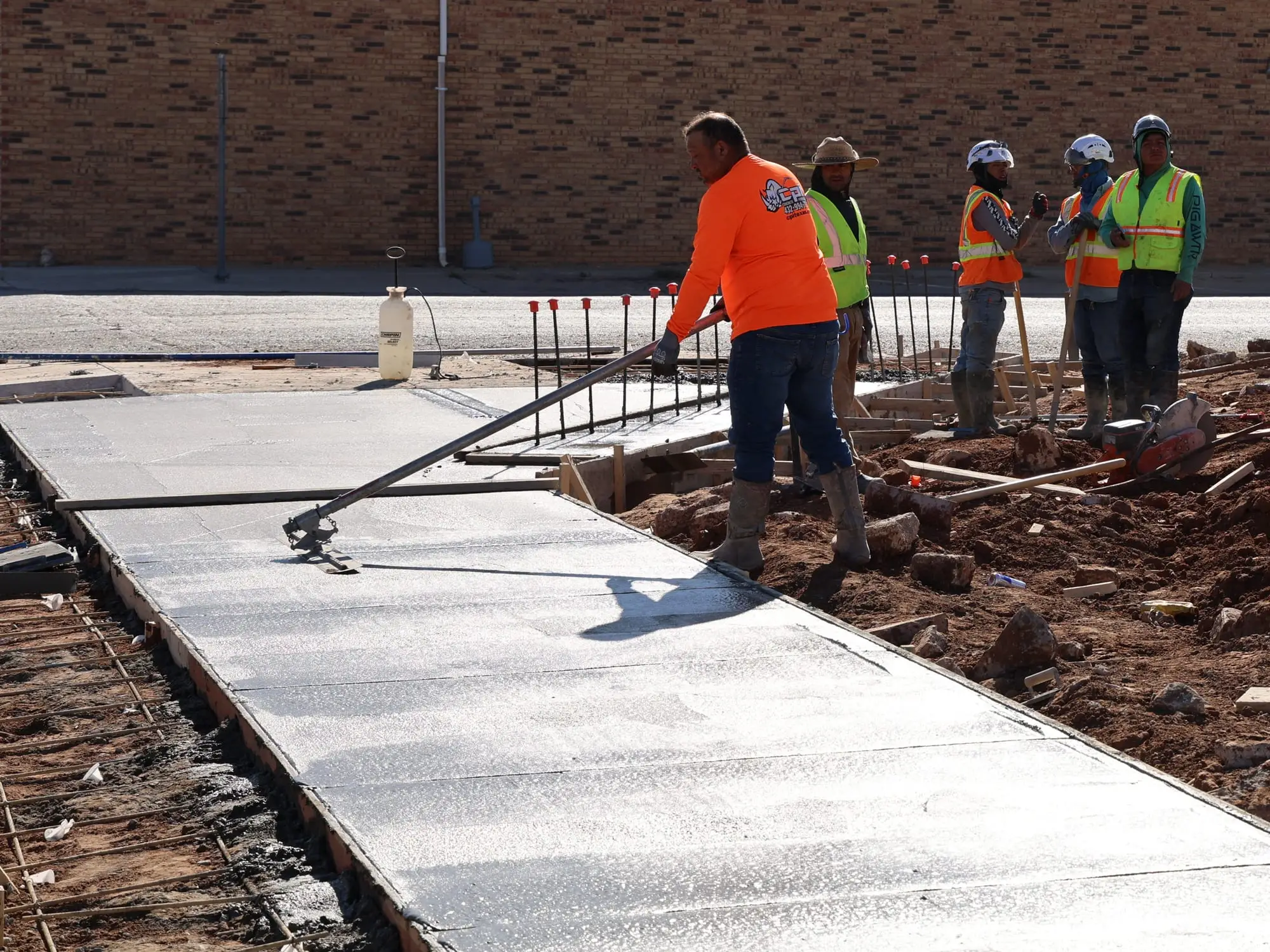 A worker pulling a screed across a fresh concrete flatwork pour