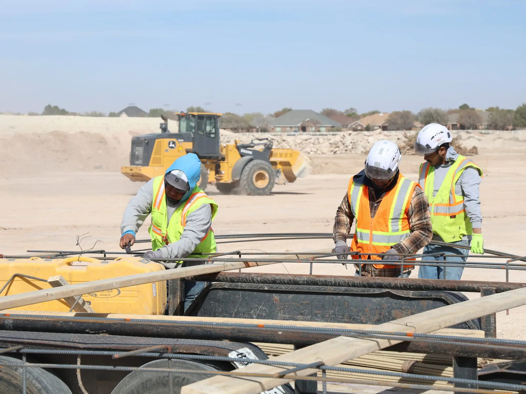 Crew members handling reinforcing steel on a trailer with a wheel loader in the background