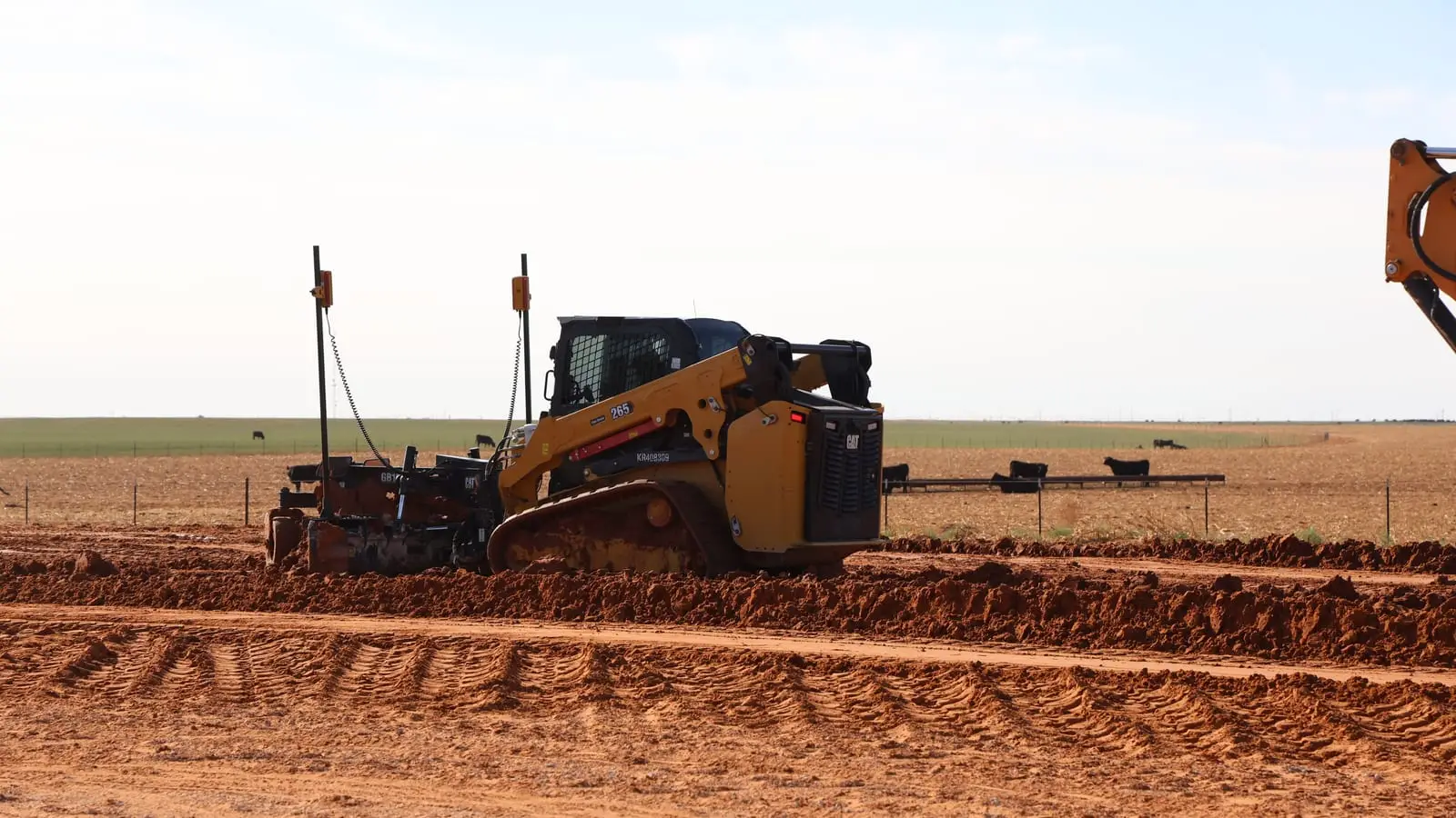 A skid steer with a grading attachment leveling red dirt on an open site