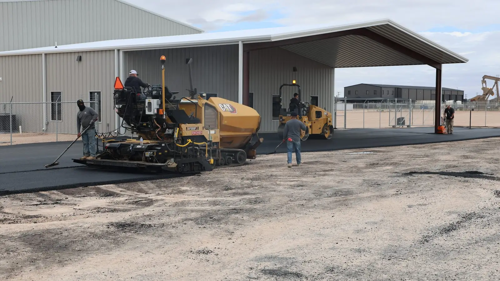 An asphalt paver laying a new surface beside a metal building